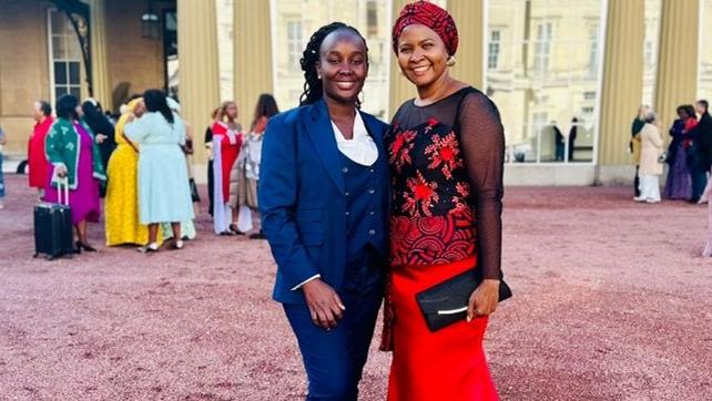 Ruth Nanjala and Anne Makena stand together outside Buckingham Palace. Other members of the UK-Kenyan community are visible in the background.